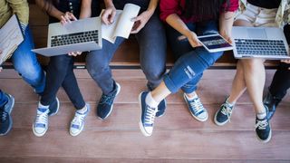 Student sat on bench using laptops, tablets and writing in notebooks